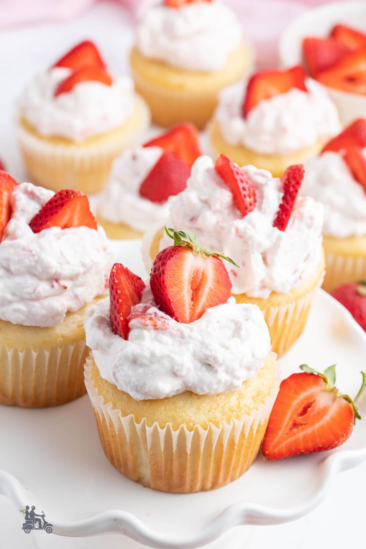 Strawberry Shortcake Cupcakes with sliced strawberries on the whipped topping and placed on a pedestal cake plate.