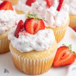 White cupcakes filled with a strawberry jam and topped with a strawberry whipped cream topping.