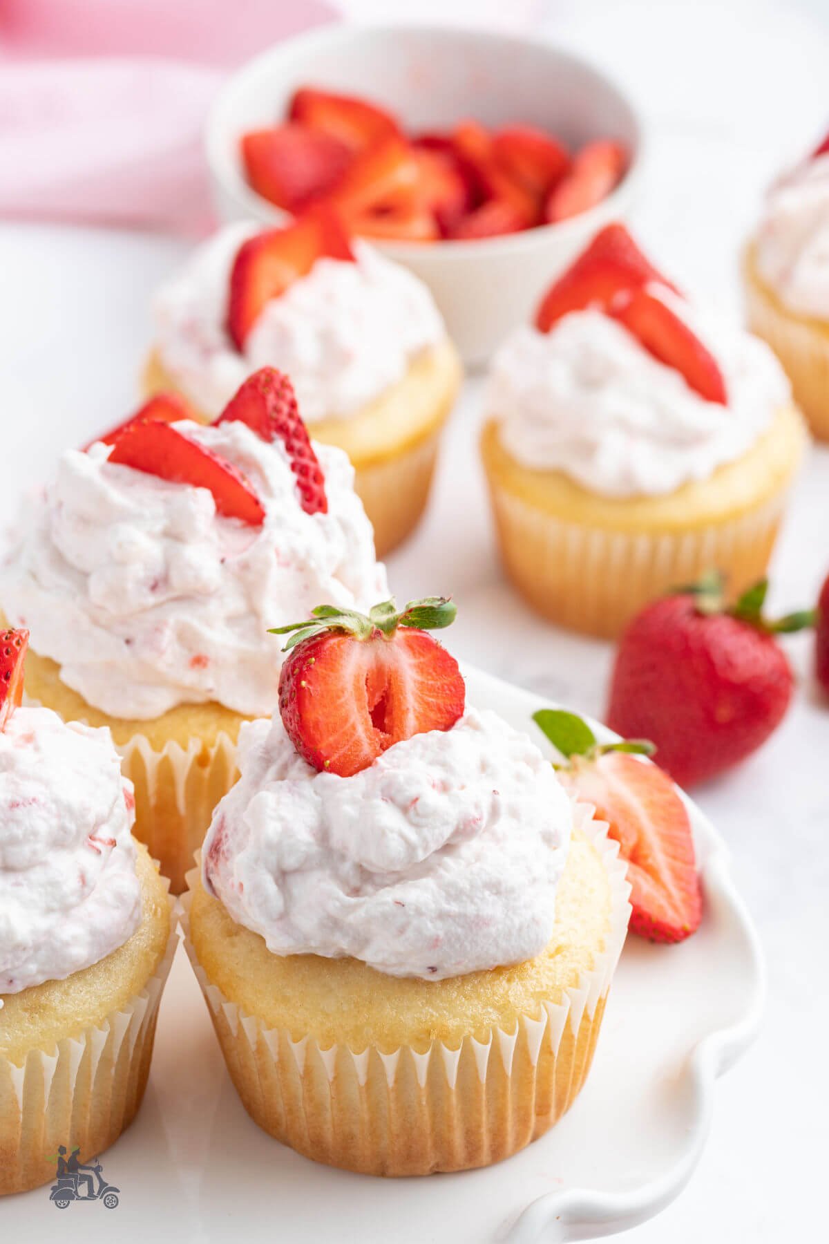 White cupcakes filled with strawberry sauce and topped with strawberry flavored whipped cream and sliced fresh strawberries. 