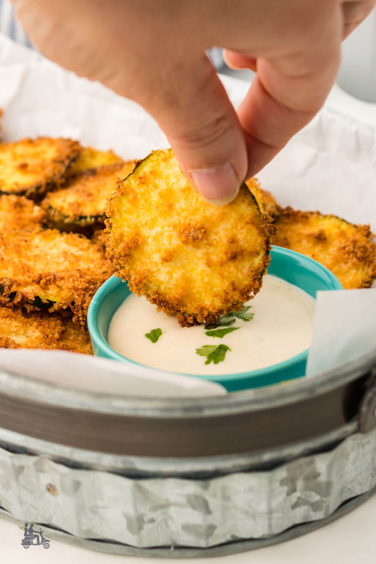 Hand dipping a zucchini chip into Ranch dressing. 