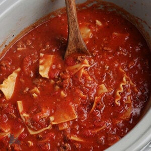 Crockpot filled with Lasagna soup and a wooden spoon stirring the soup.