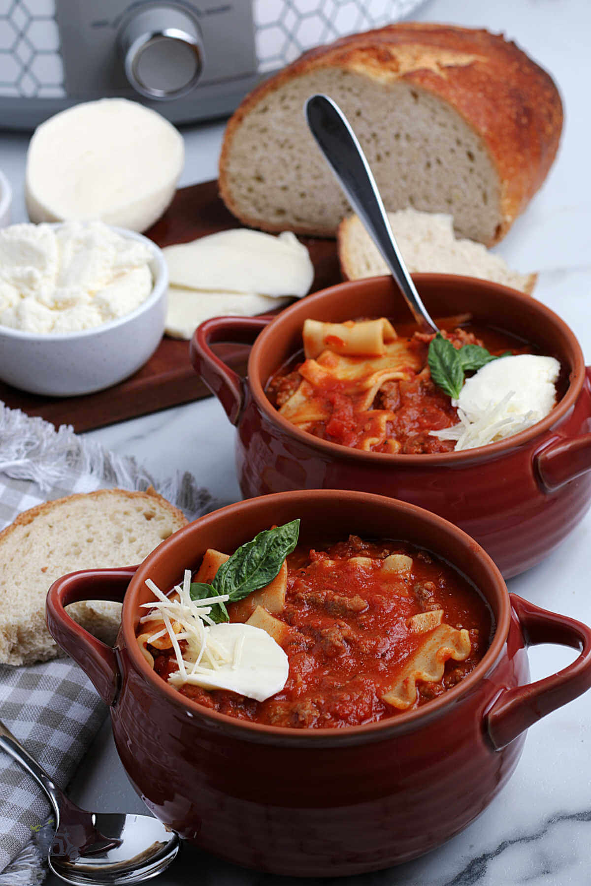 Two bowls filled with red lasagna soup garnished with ricotta cheese and a basil sprig. 