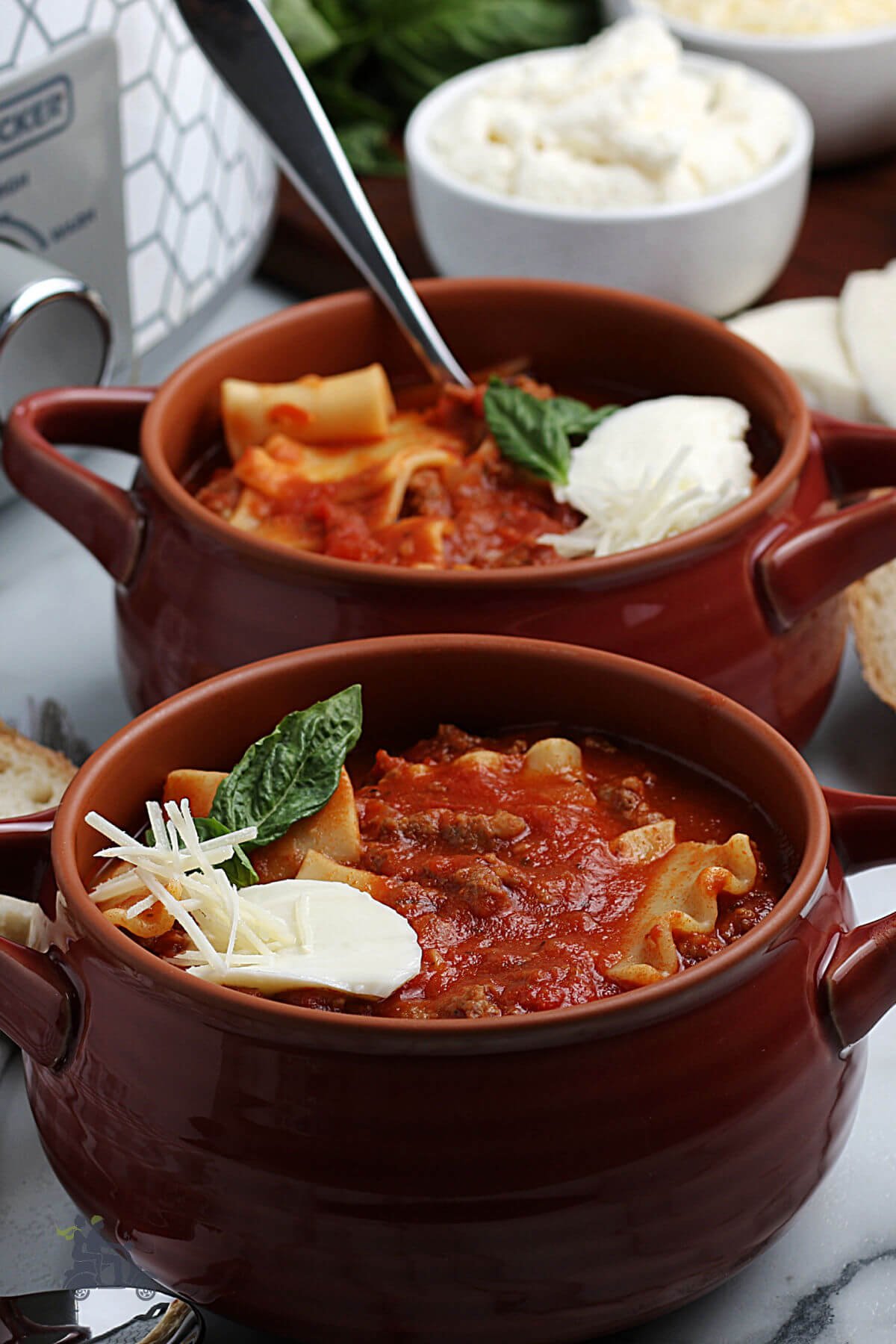 Side view of the slow cooker made lasagna soup garnished with mozzarella cheese and basil sprig. 