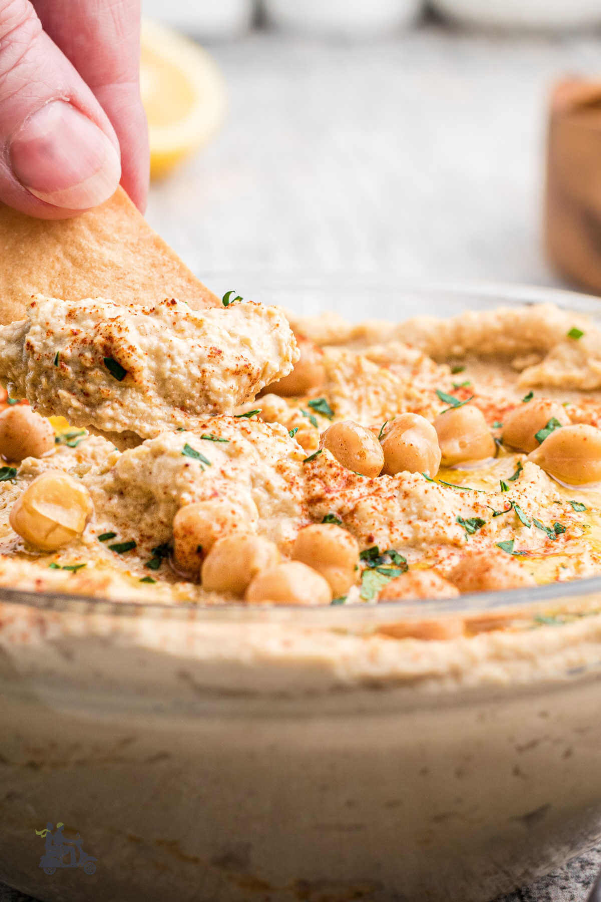 A hand dipping a pita chip into the bowl of homemade hummus. 