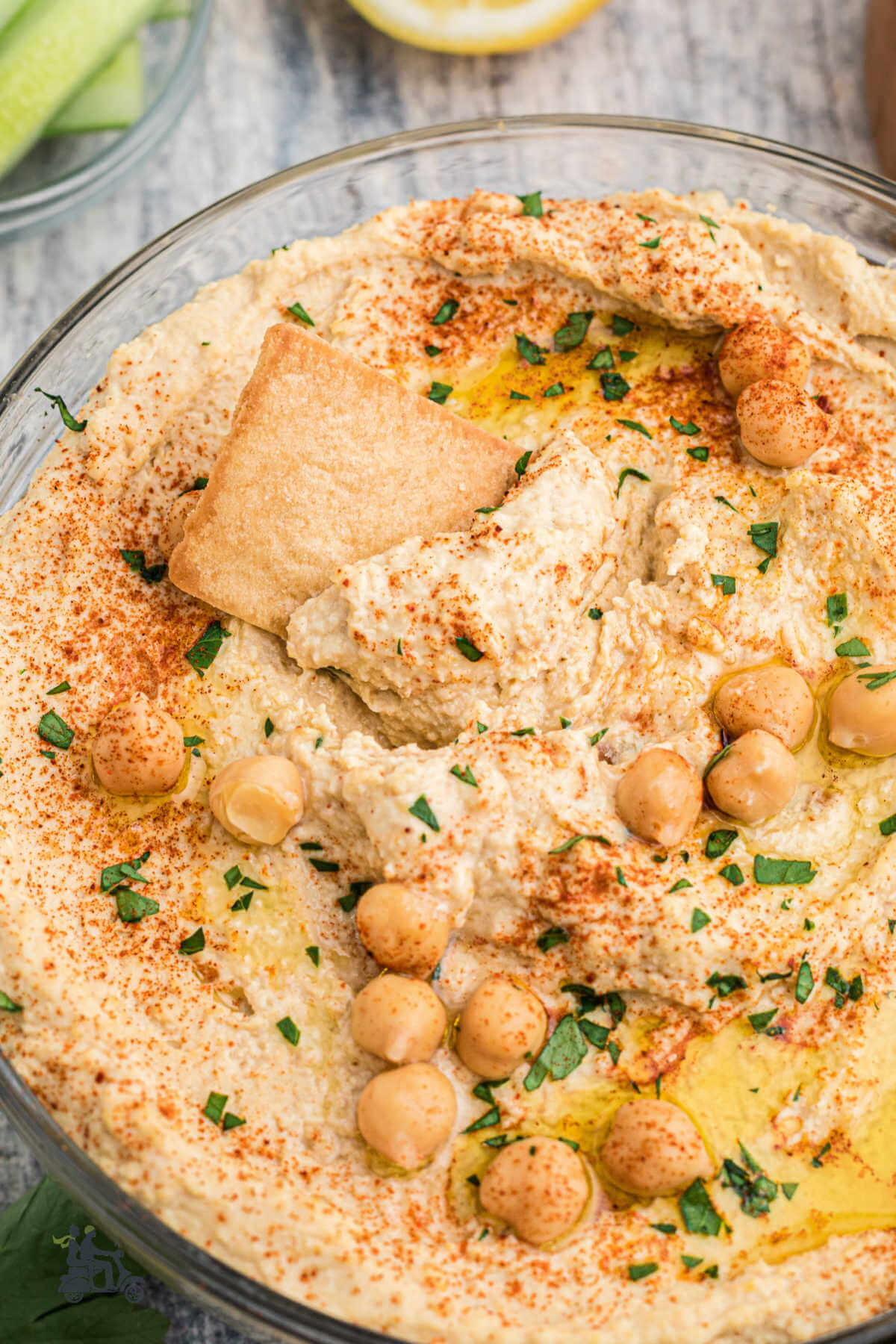 A large bowl of chickpea hummus with a pita chip stuck in the creamy dip. 