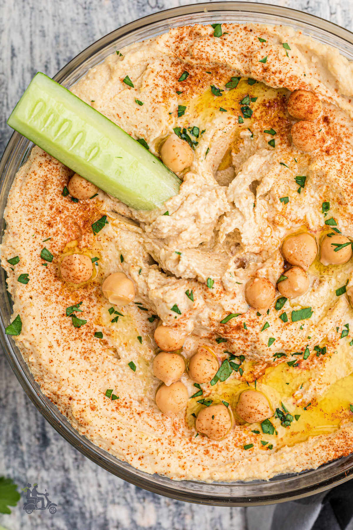 A cucumber spear stuck in the middle of a creamy bowl of chickpea hummus. 