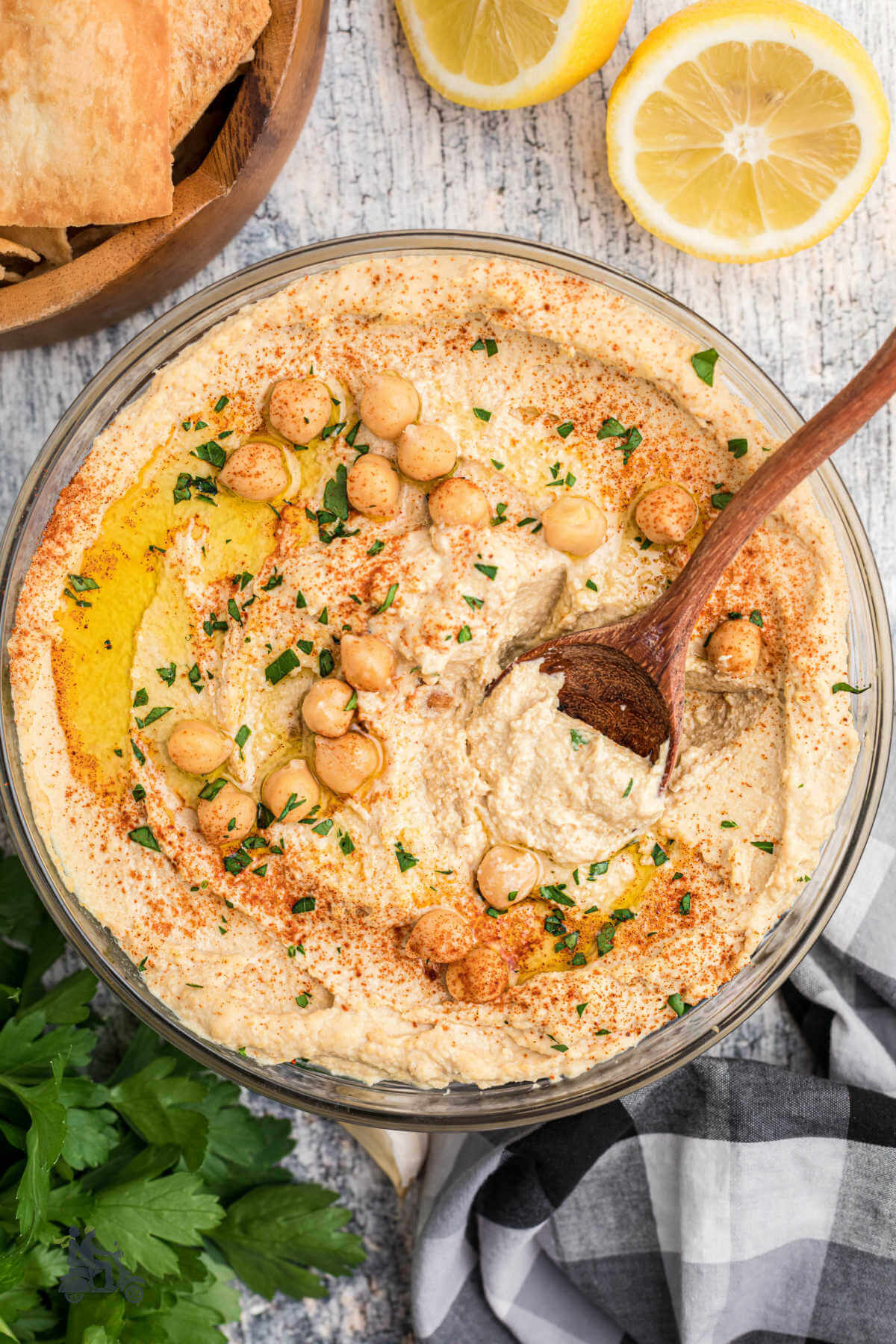 Homemade hummus in a glass bowl with a wooden spoon stuck in the creamy dip. 