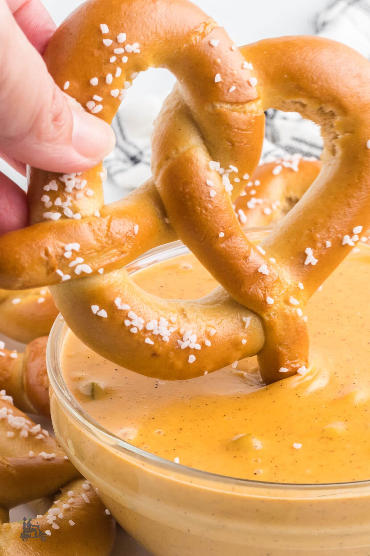 A soft pretzel dipped into a bowl of cheesy dipping sauce with jalapeños. 