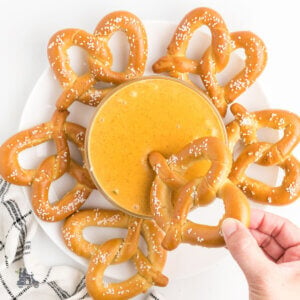 A glass bowl filled with spicy cheese dipping sauce and a pretzel dipped into the creamy cheese.