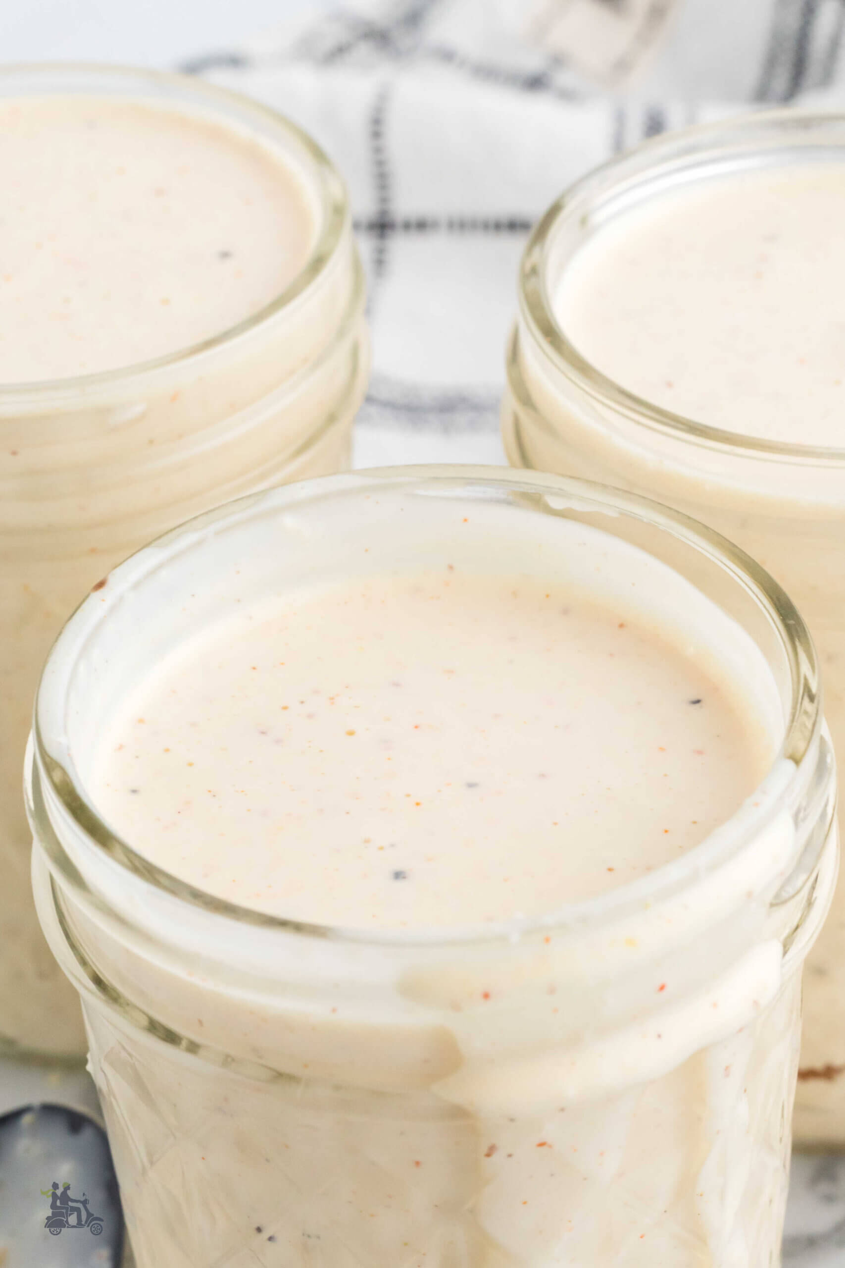 Three glass jelly jars with homemade Alabama white sauce with some sauce dribbling down the side. 