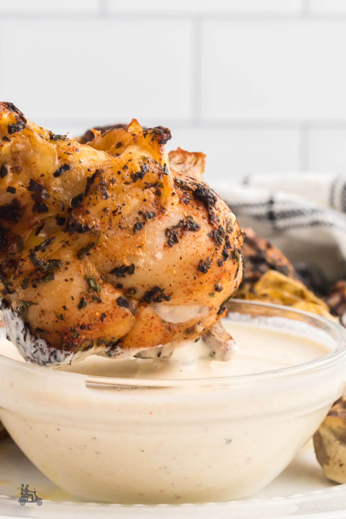 A grilled chicken wings dipped into the Alabama White sauce in a small bowl. 