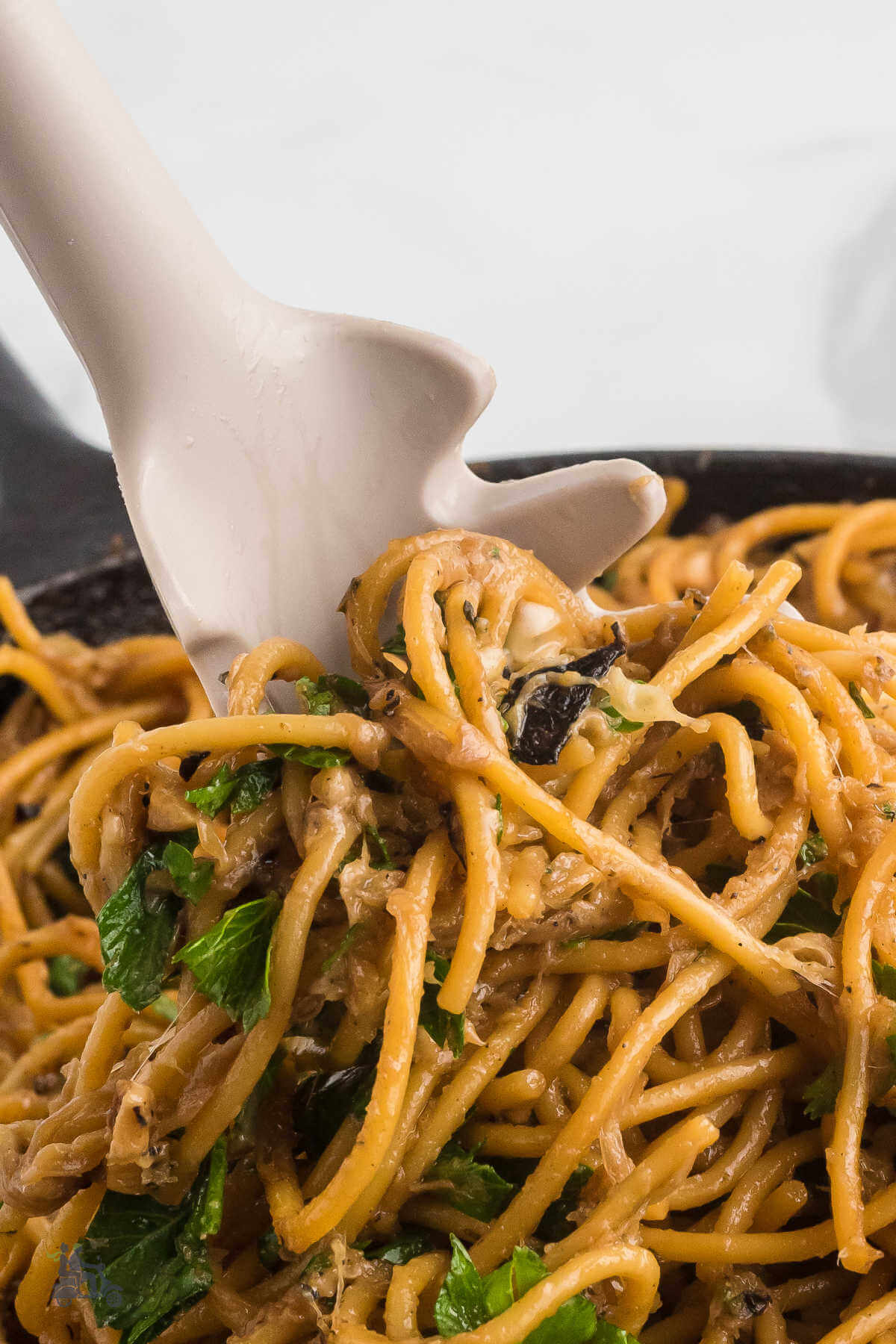 A pasta spoon grabbing some spaghetti strands sprinkled with chopped Italian parsley. 