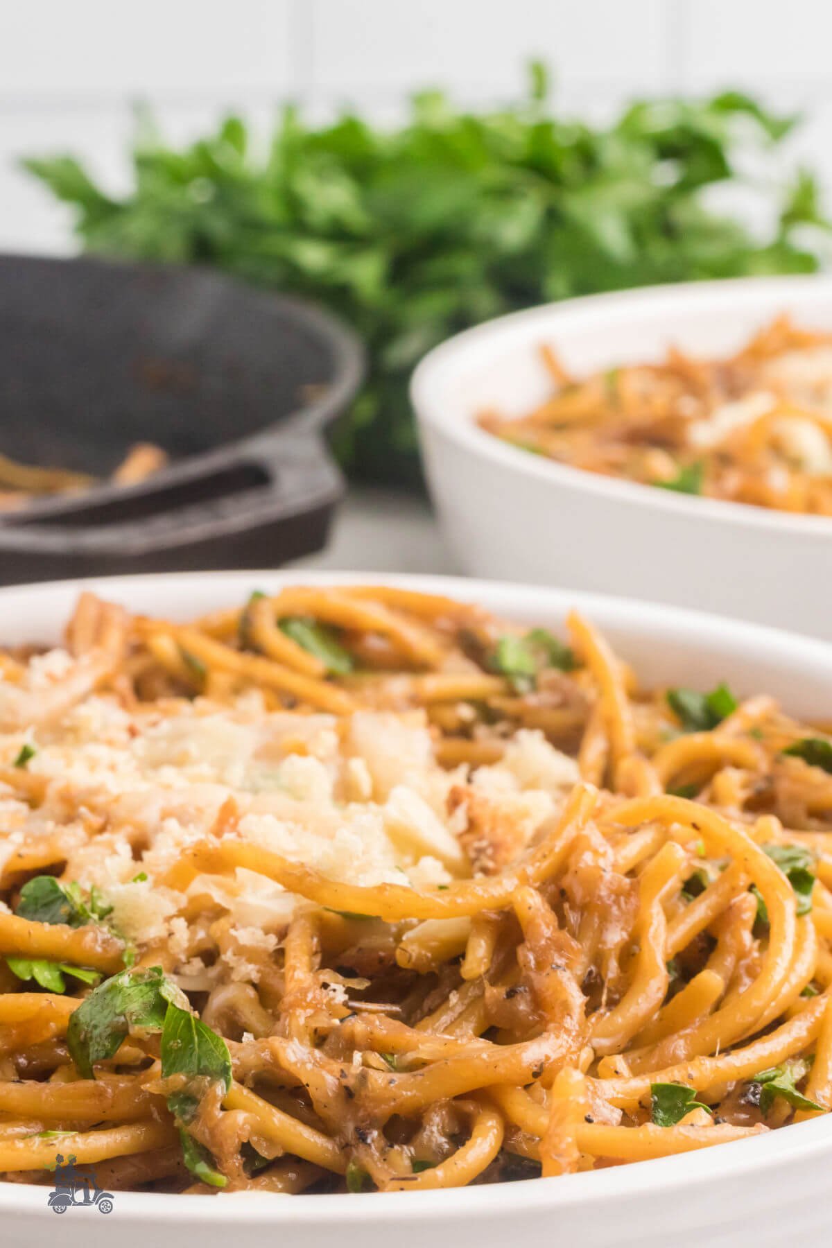 Spaghetti flavored with beef stock and caramelized onion with melted cheese on top all served in a white bowl. 