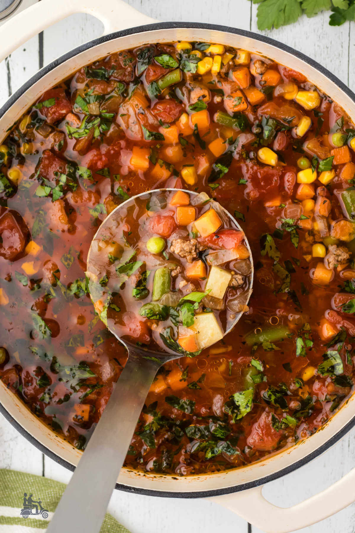 Ladle holding a scoop of hamburger vegetable soup with potatoes. 