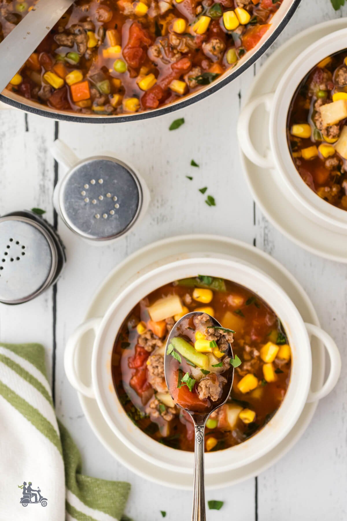 Two white ceramic bowls filled with vegetable hamburger soup recipe and salt and pepper on the side. 