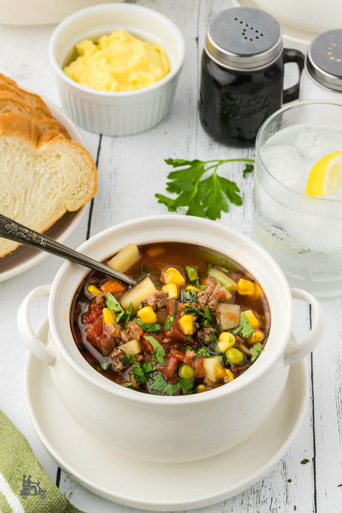 A bowl of Hamburger vegetable soup with potatoes and bread and butter on the side. 