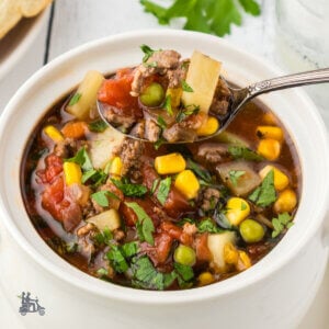 Closeup of a white ceramic bowl filled with a vegetable hamburger soup with potatoes.