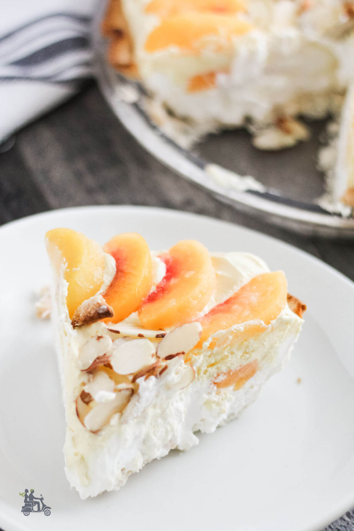 A slice of the creamy peach pie with whipped topping and almonds on a white plate. 