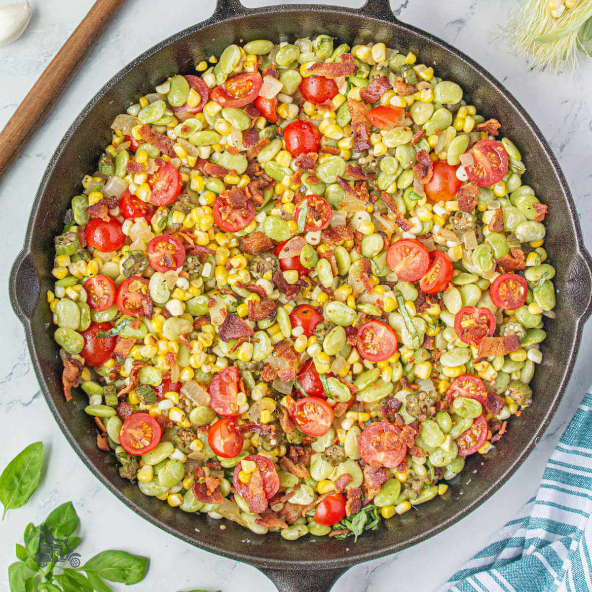 Black cast iron skillet filled with corn succotash and mixed with lima beams and cherry tomatoes.