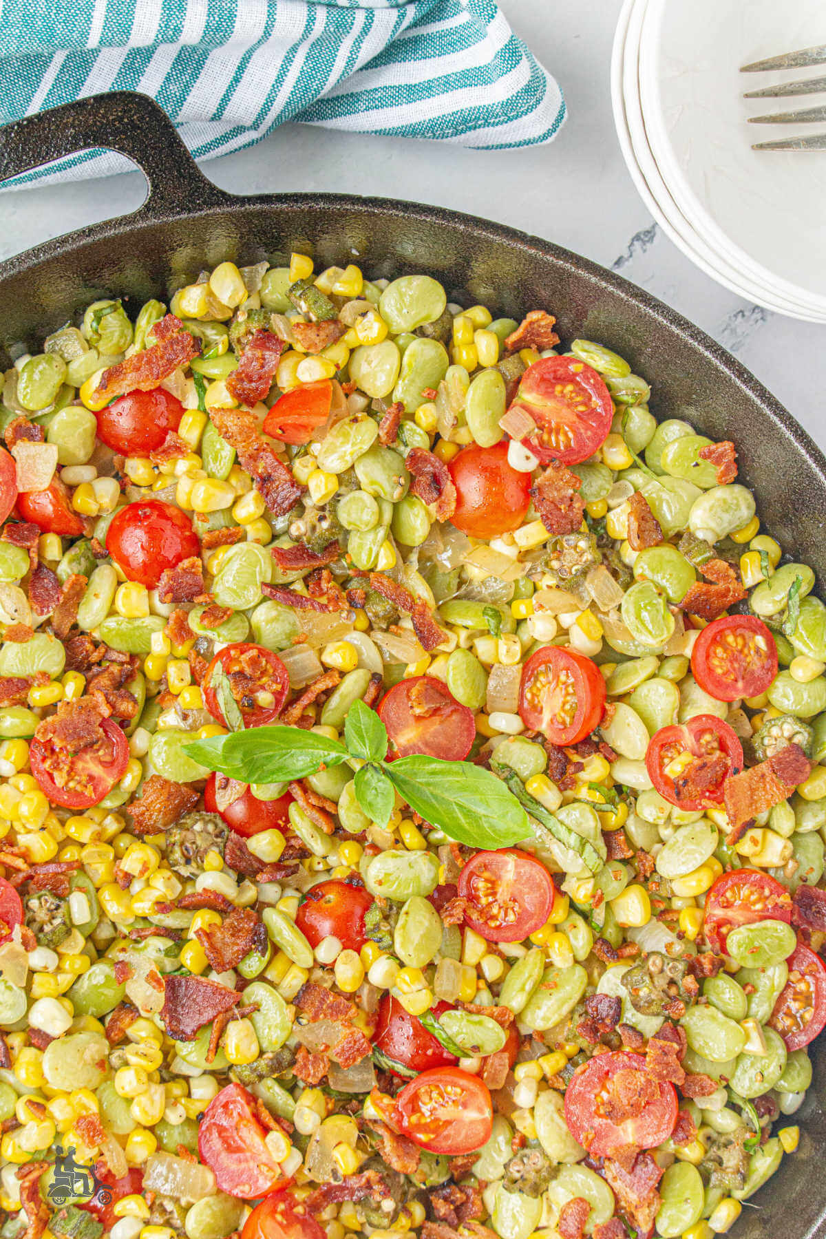 Skillet filled with corn succotash with basil leaf in the center. 