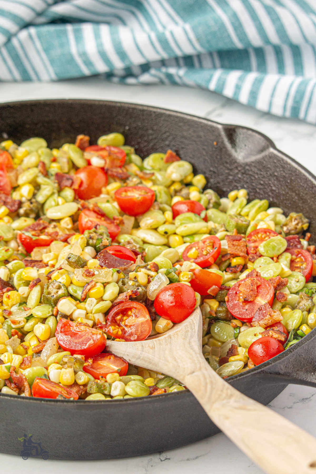 Black cast iron skillet with the finished corn succotash vegetable dish topped with halved cherry tomatoes. 