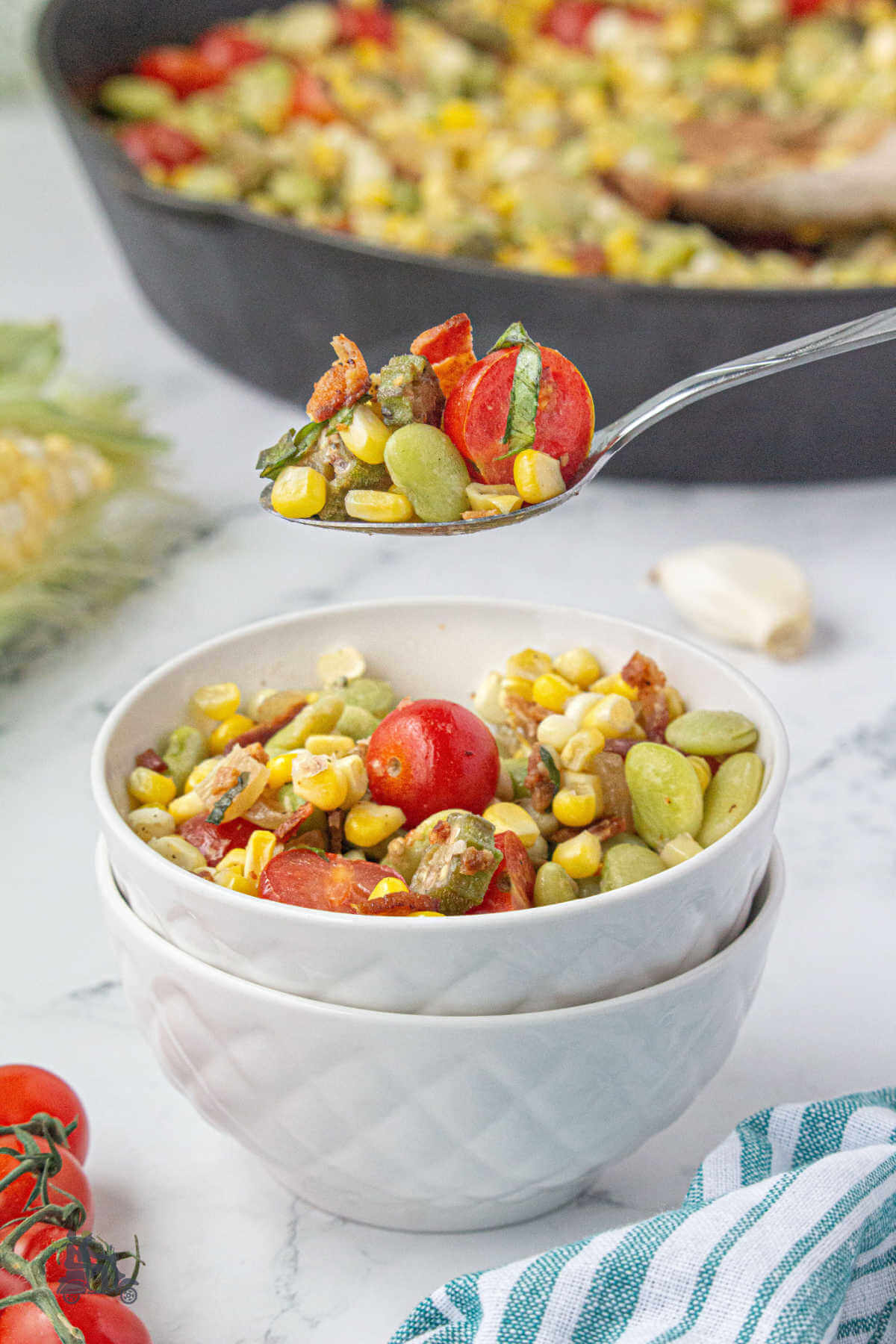 A spoon holding a bite of corn succotash with bacon, tomatoes, and fresh basil. 