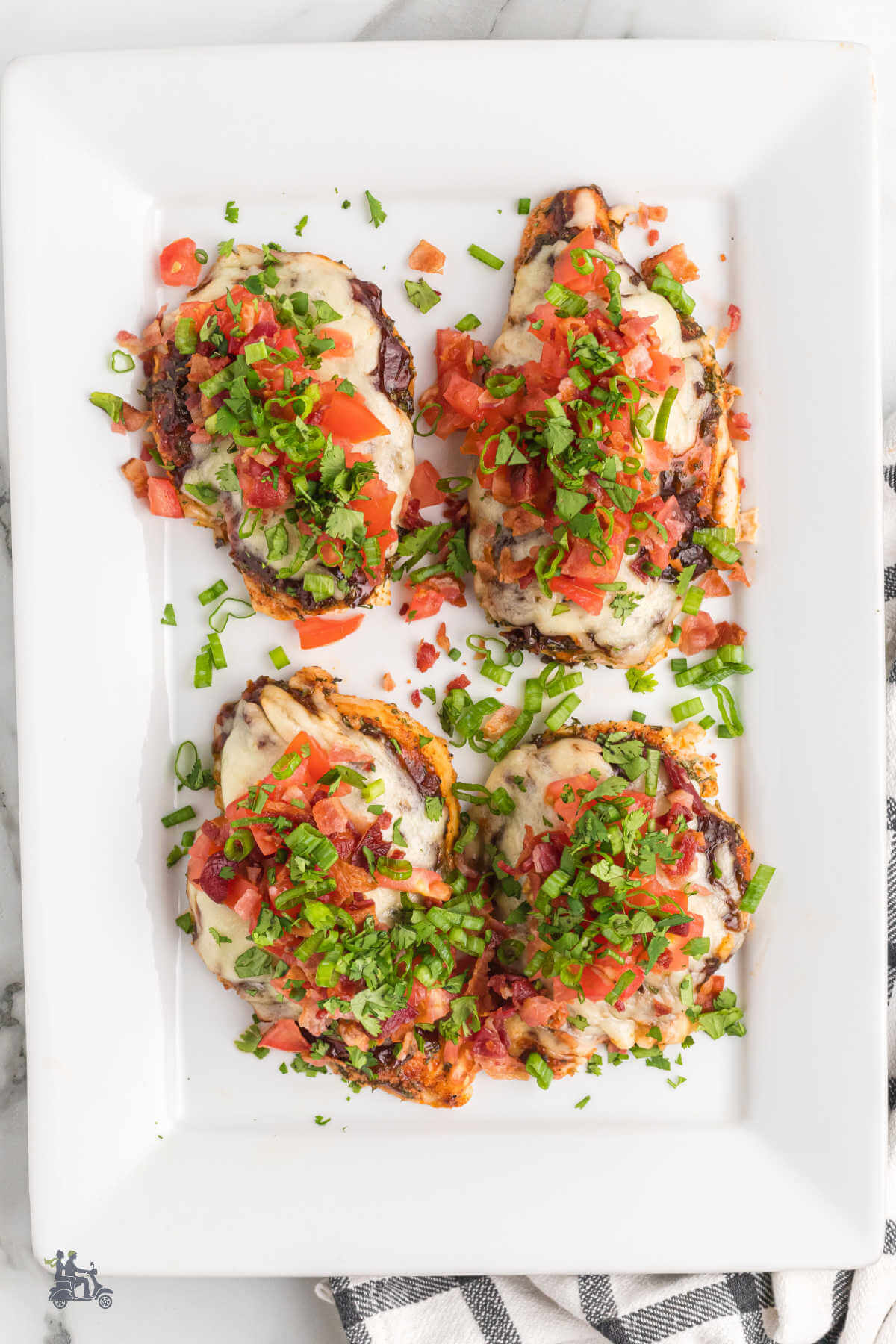 A white baking dish with the complete recipe of Chicken Monterey consisting of chicken breast, covered in cheese, diced tomatoes, and green onions. 