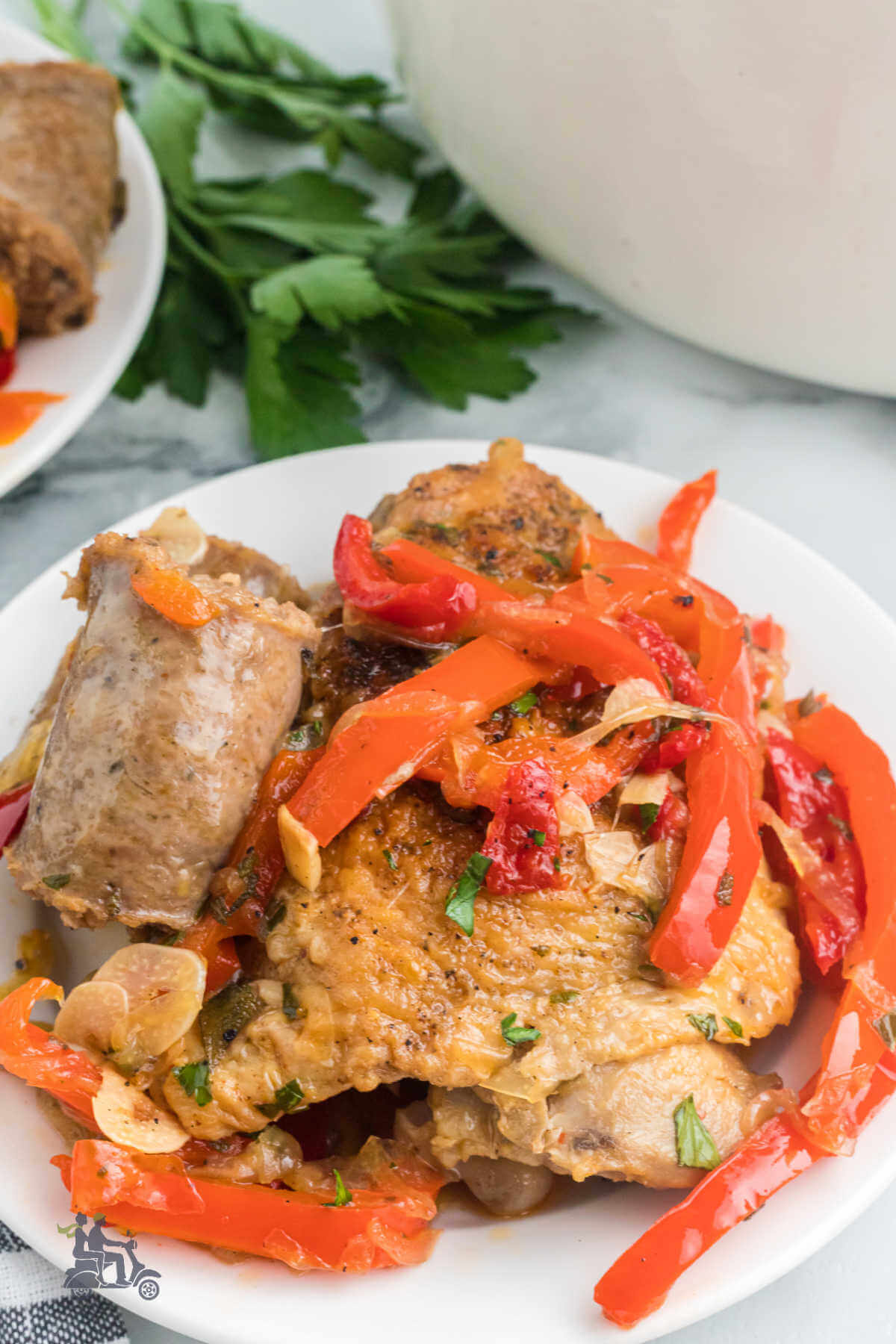 A white plate with a serving of chicken scarpariello which features braised chicken thighs, red peppers, and onion in a rich flavorful sauce. 