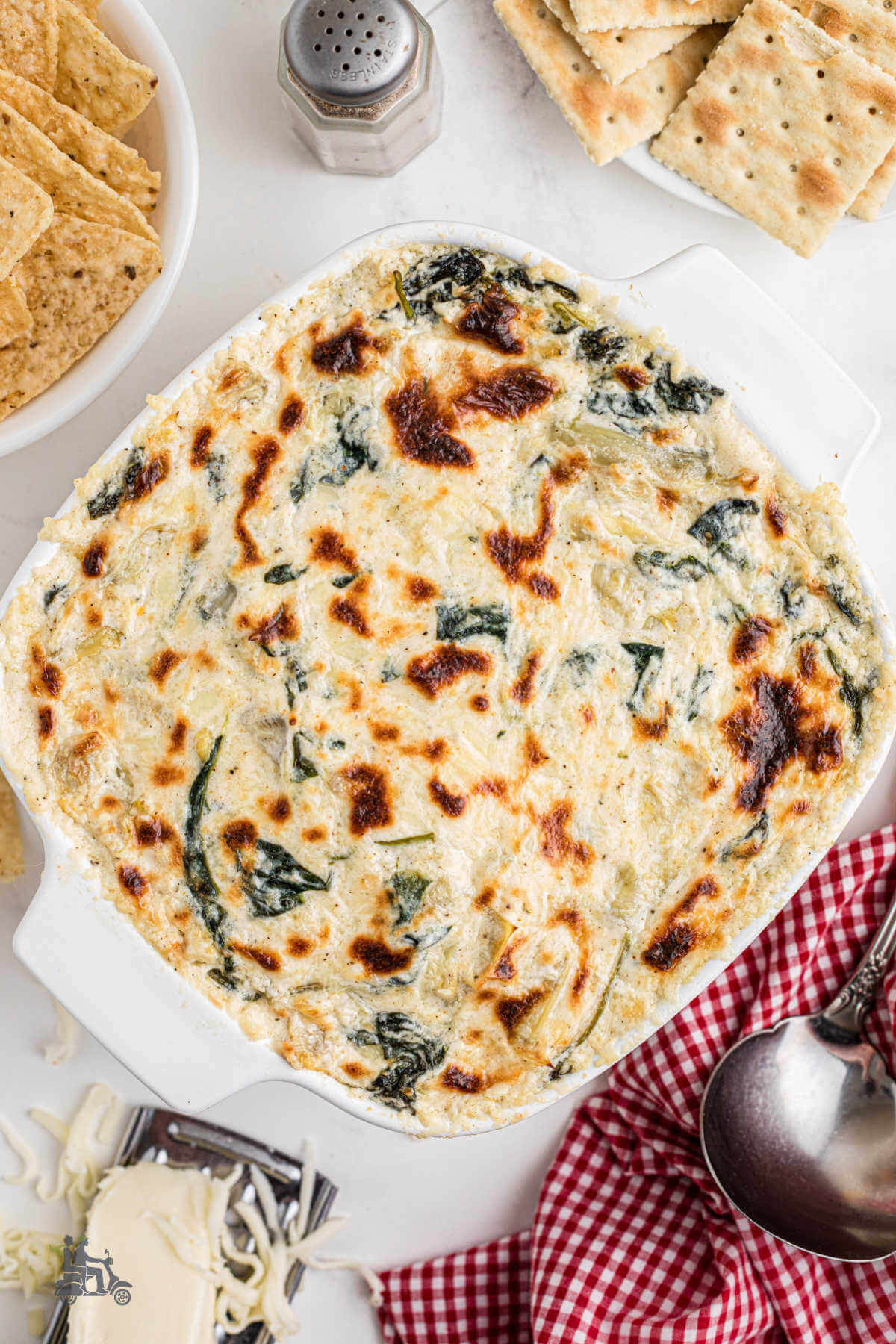 White Casserole dish filled with baked cream cheese spinach and artichoke hot dip. 