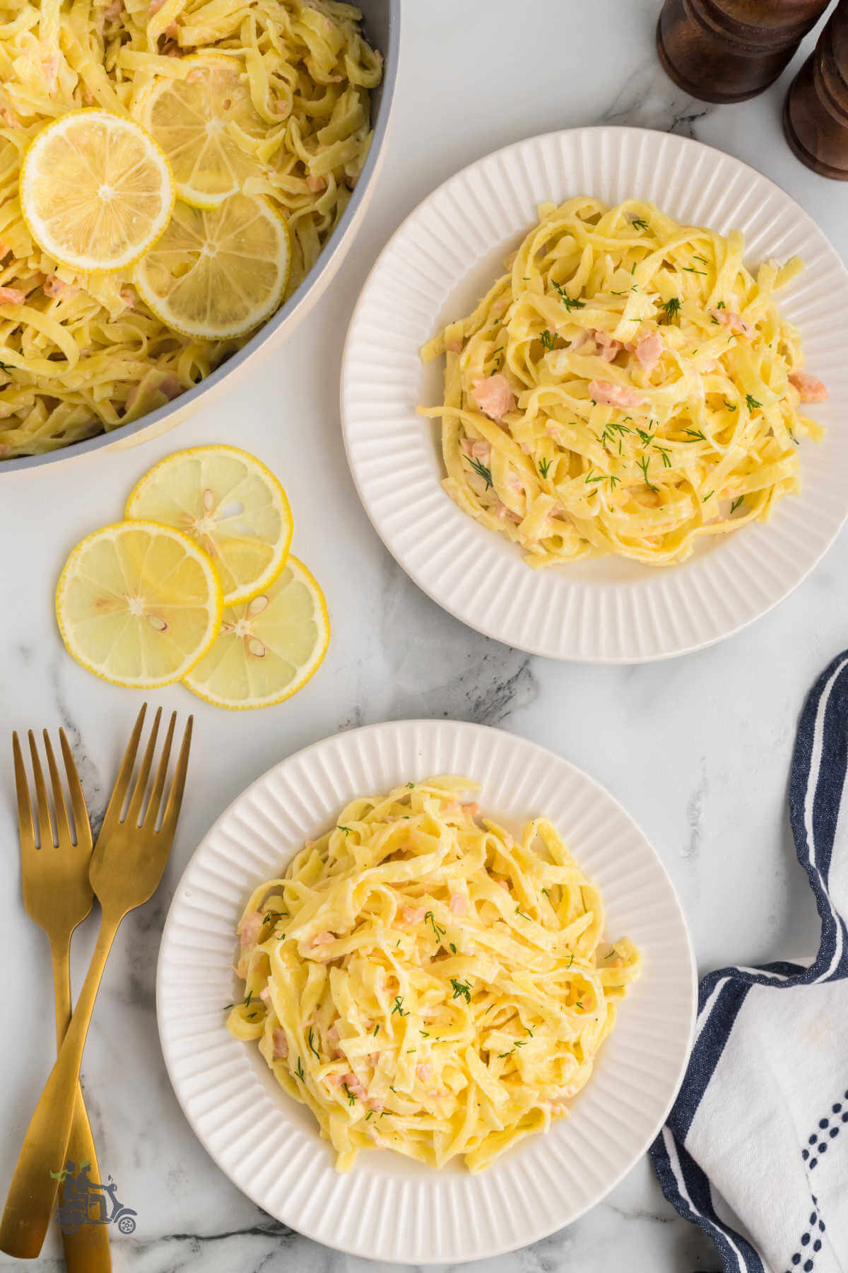 Two white plates with servings of tagliatelle al salmone with fresh dill sprinkled on top.
