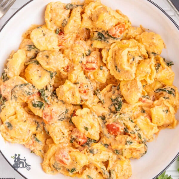 A skillet filled with cheese tortellini covered in a creamy sauce with spinach and tomatoes.