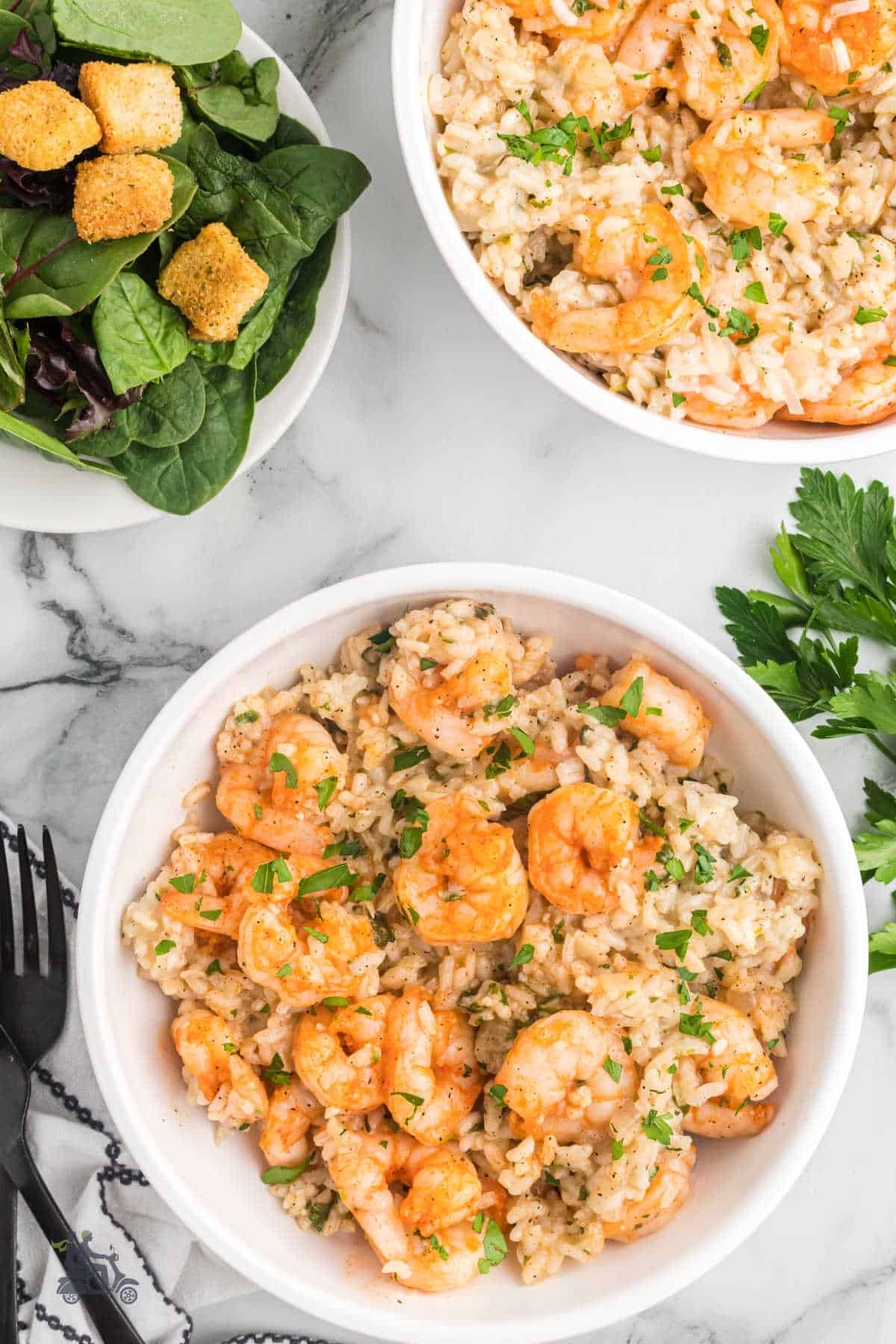 Shrimp Risotto in a white bowl and topped with a sprinkle of chopped basil. A spinach salad is to the side of the rice dish. 