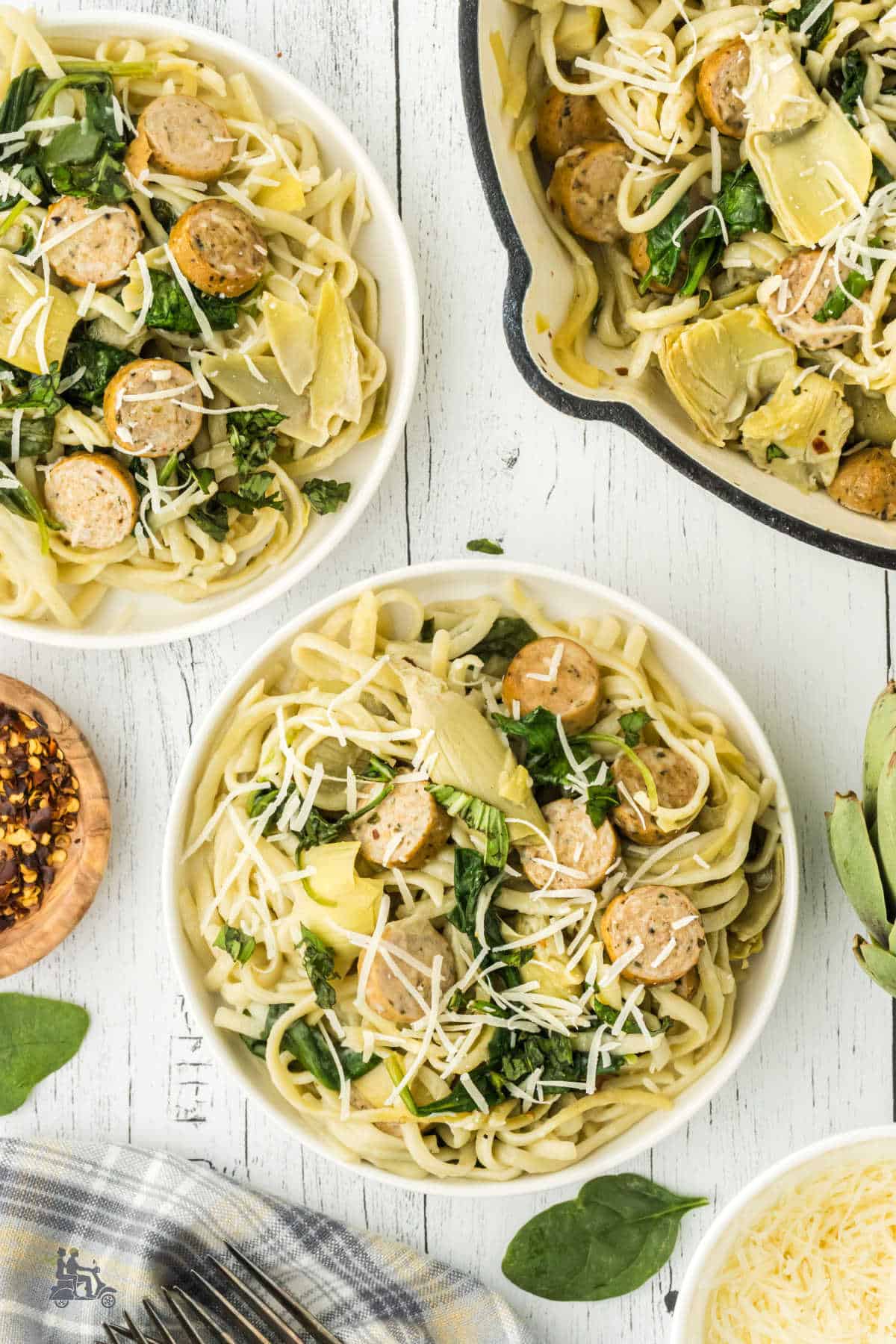 Two bowls filled with chicken sausage and pasta with artichoke hearts, spinach, and parmesan cheese. 