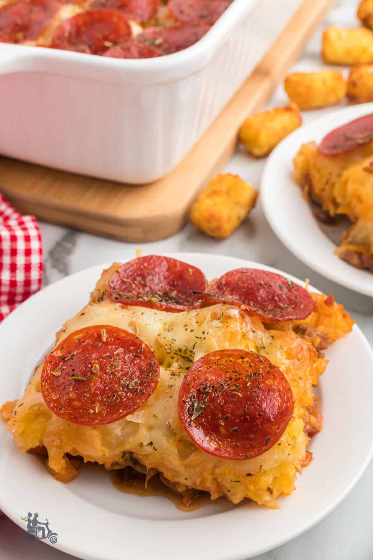 A square of three meat potato tater tot pizza with mozzarella and pepperoni on a white plate. 