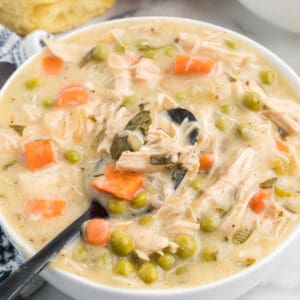 A white bowl filled with homemade chicken pot pie with a soup spoon drawing up a spoonful.