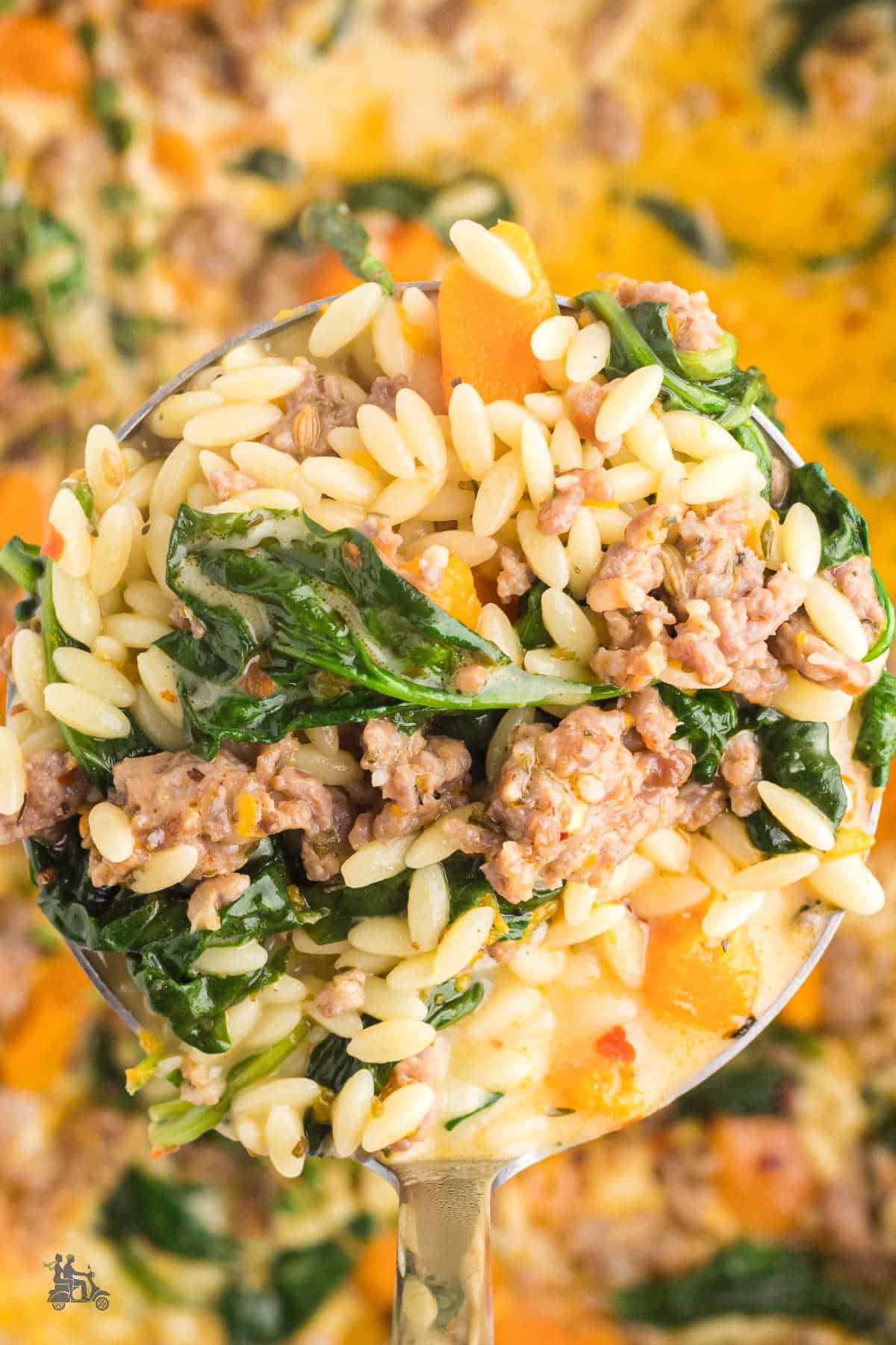 Ladle overflowing with the soup's orzo, sausage, spinach, and butternut squash. 