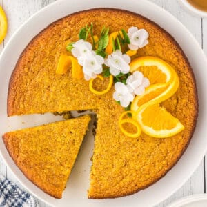 Flourless Orange Almond Cake with a slice cut and an orange slice garnish on top with orange blossoms.
