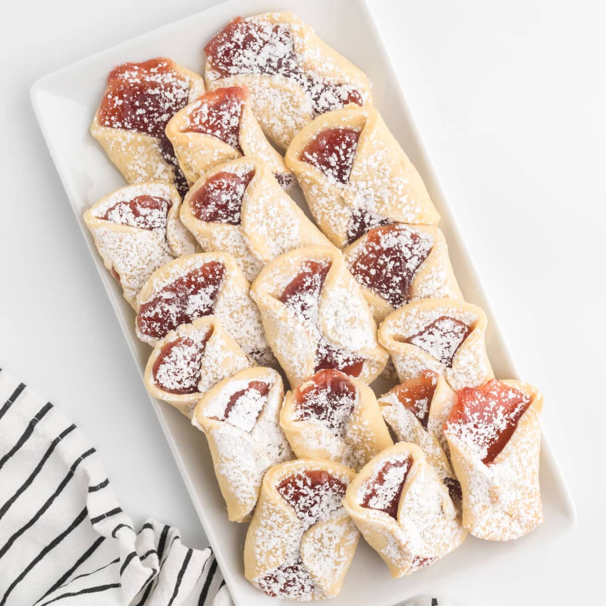 A white dessert plate filled with pizzicati, which are Italian pinch cookies filled with strawberry jam or nutella.