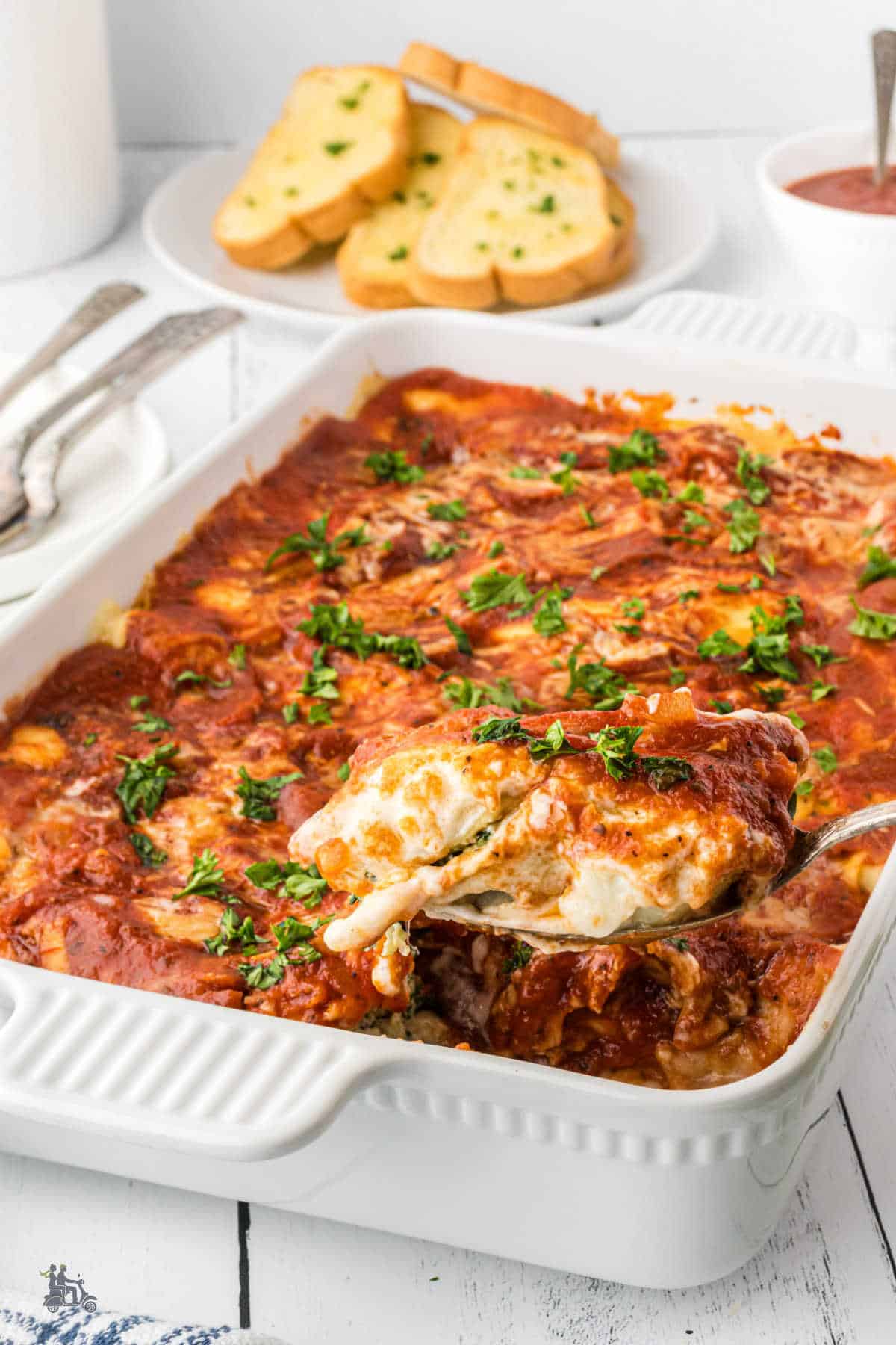 A white casserole baking dish holding the Three-cheese Cannelloni with Spinach recipe topped with marinara sauce. 