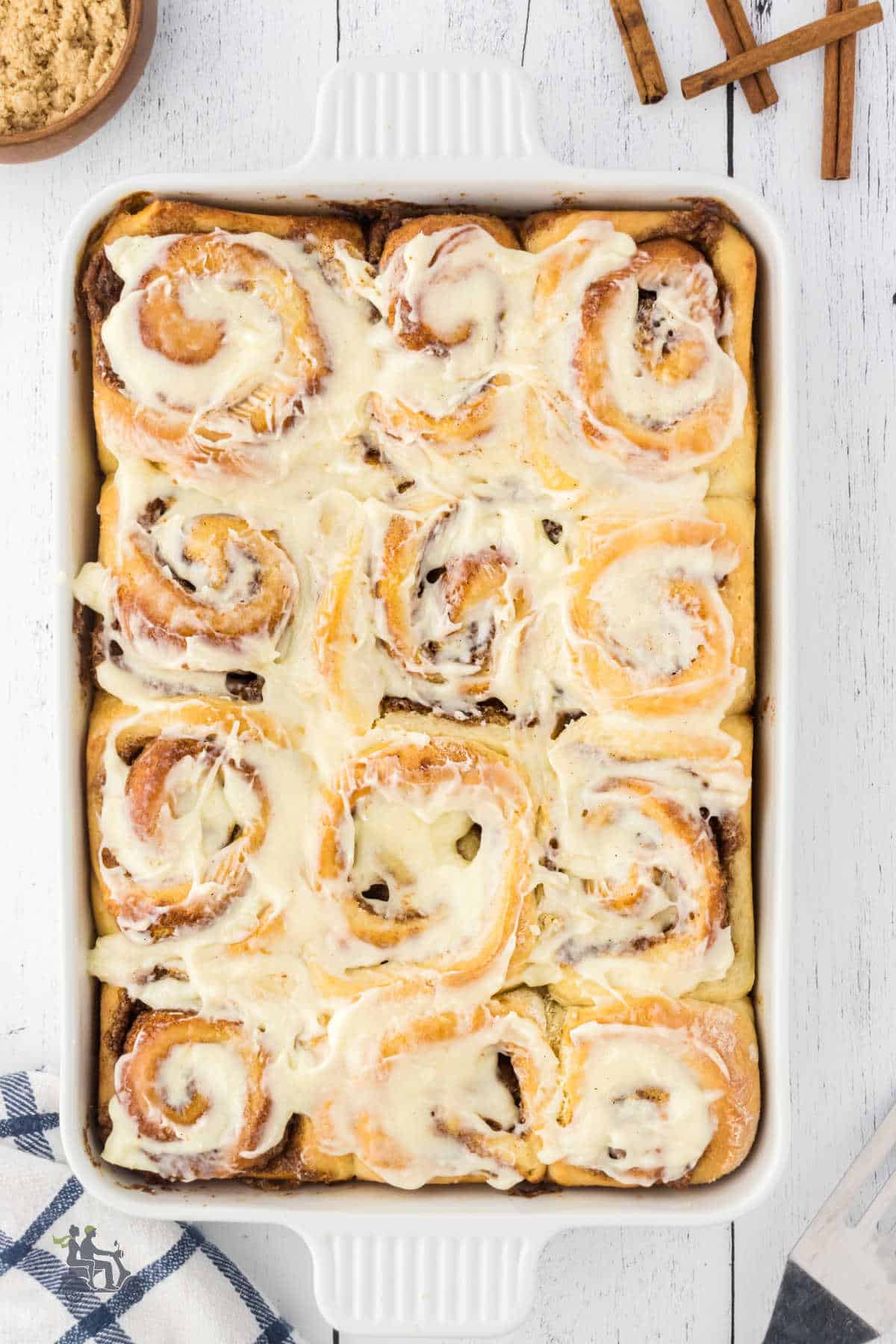 Homemade cinnamon rolls in a white baking dish are frosted and ready to eat. 