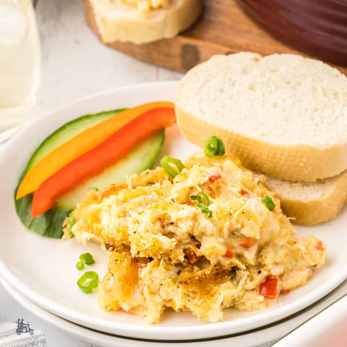 Crab au Gratin on a white plate with slices of white bread, cucumber slices, and red pepper stick.