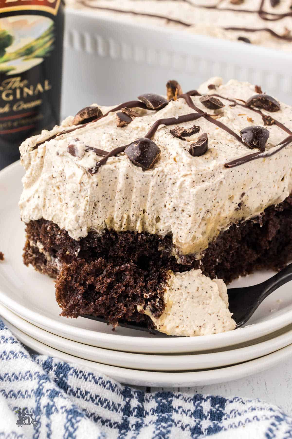 A fork cuts into the chocolate poke cake square showing the thick Bailey's Irish Cream flavored whipped cream topping. 