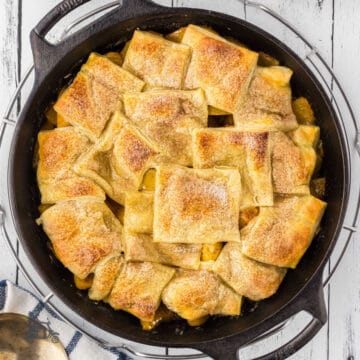 Canned peaches are made into a peach cobbler with a puff pastry top, all in a black cast iron skillet.