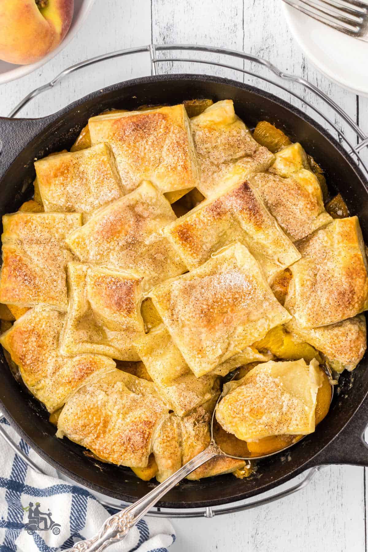 Peach cobbler in a black cast iron skillet with a spoon, removing a serving. 