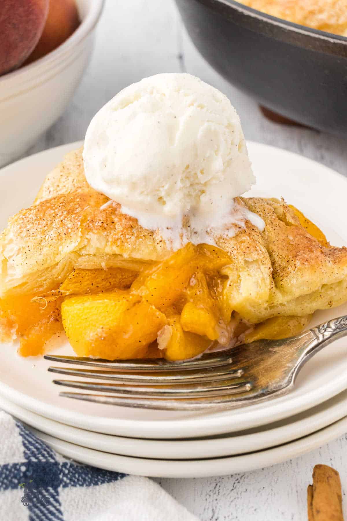 Baked peach dessert with pastry top and scoop of vanilla ice cream on top. 