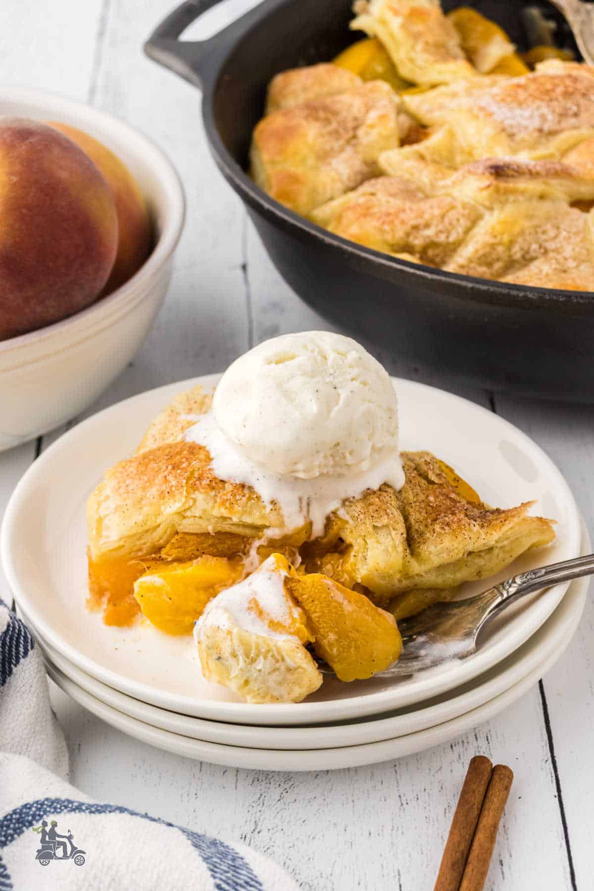 Peach Cobbler is made with canned peaches, a puff pastry top on a white plate, and a dessert topped with a scoop of vanilla ice cream. 