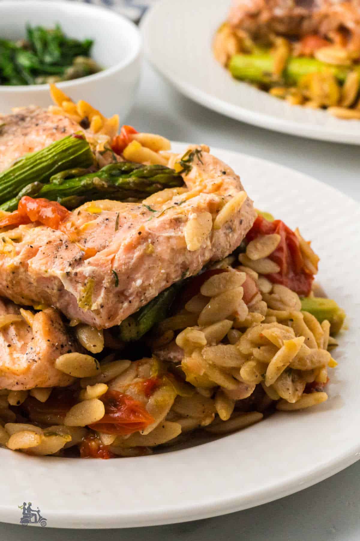 Baked Salmon sits on top of cooked orzo with asparagus and tomatoes mixed in with the pasta. 