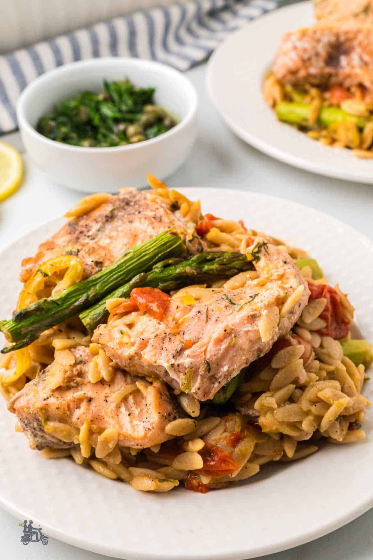A serving of Lemony Salmon and Orzo Pasta with Asparagus on a white plate with the dill caper sauce on the side. 