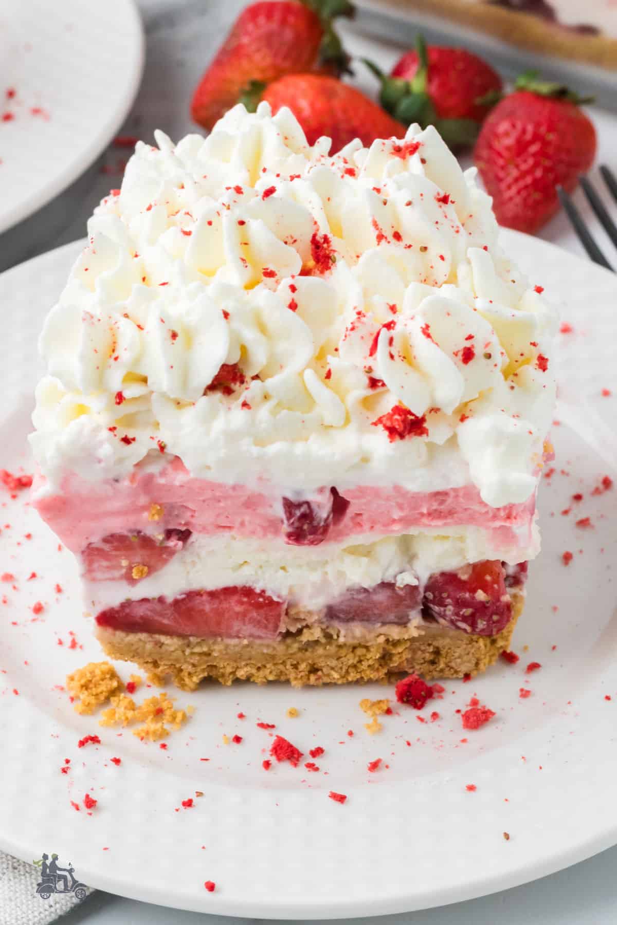 No-bake dessert made into four layers with graham crackers on the bottom, strawberries on top of the crust, and whipped strawberry cream in the middle.