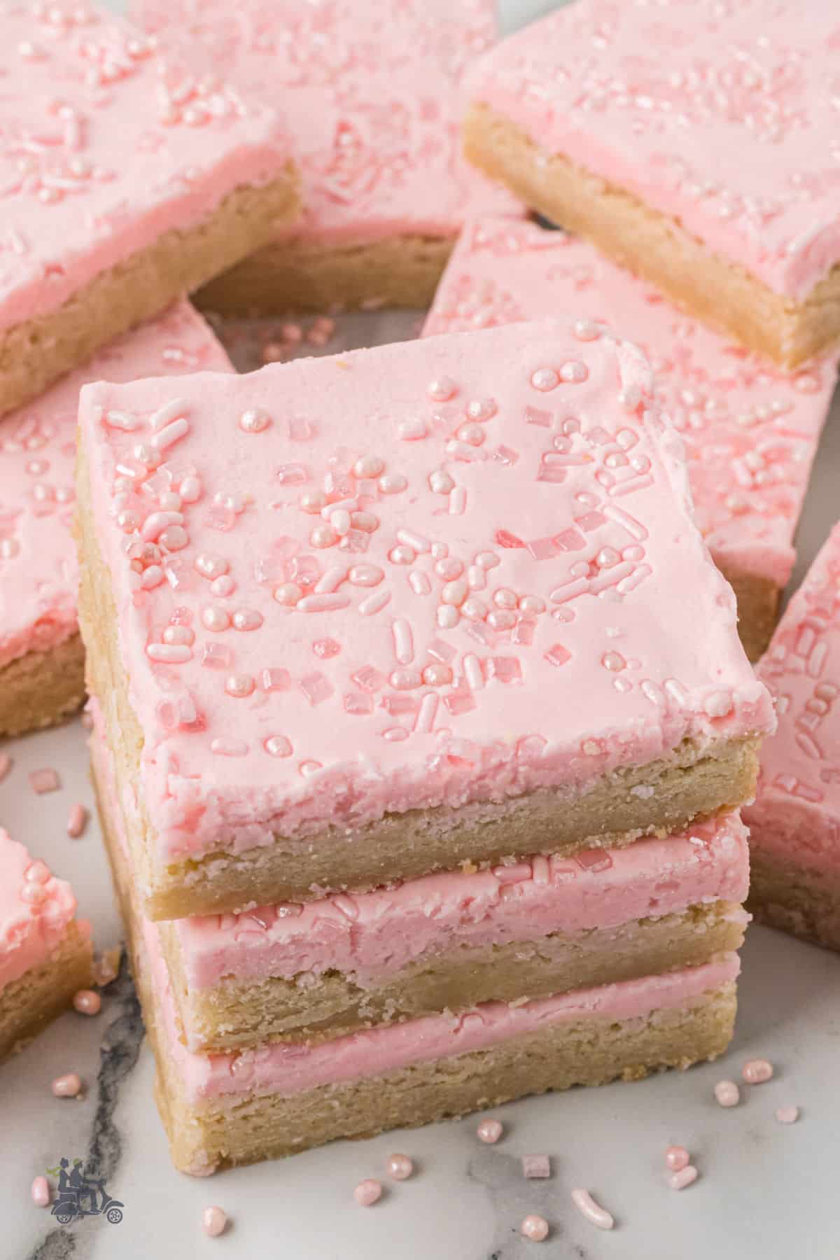 Pink Frosted Sugar Cookie bars with pink sprinkles stacked on top of each other